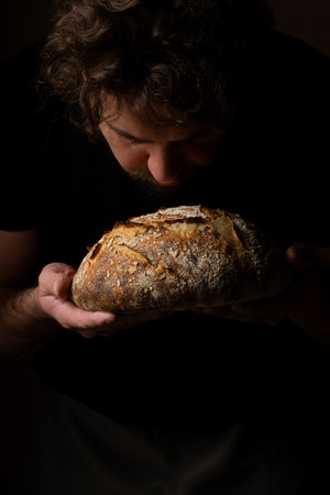 Attractive young Caucasian chef posing with white sourdough bread. The sourdough bread is the central protagonist of the scene, standing out with beautiful golden tones against the dark background.の写真素材