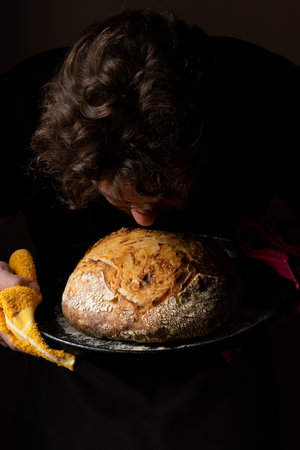 Attractive young Caucasian chef posing with white sourdough bread. The sourdough bread is the central protagonist of the scene, standing out with beautiful golden tones against the dark background.の写真素材
