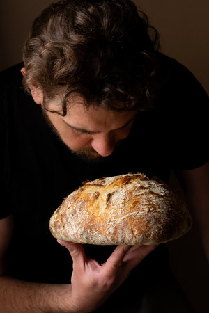Attractive young Caucasian chef posing with white sourdough bread. The sourdough bread is the central protagonist of the scene, standing out with beautiful golden tones against the dark background.の写真素材
