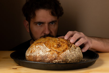 Attractive young Caucasian chef posing with white sourdough bread. The sourdough bread is the central protagonist of the scene, standing out with beautiful golden tones against the dark background.の写真素材