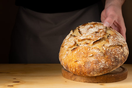 The hands of a young man handling sourdough bread, highlighting the bread with beautiful golden tones against the dark background.の写真素材