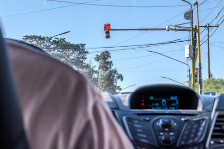View from behind a car, of a red light, a camera and street lighting cables.
