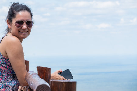 Latina tourist girl contemplating the view from a high viewpoint. She has glasses and a cell phone in her hand.の写真素材
