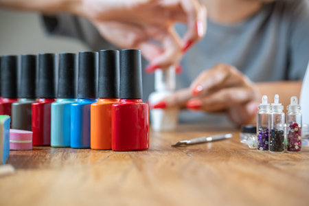 Colored nail polishes with a background of a woman painting her nails on a table with many accessories for work.の写真素材