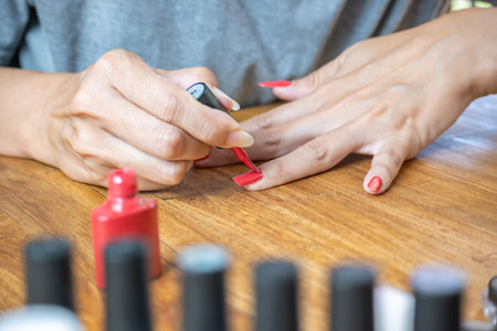 Hands of a young Latin woman painting her nails with a red polish on the table, surrounded by accessories for painting.の写真素材