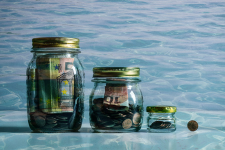 glass jars filled with coins to different levels underwaterの写真素材