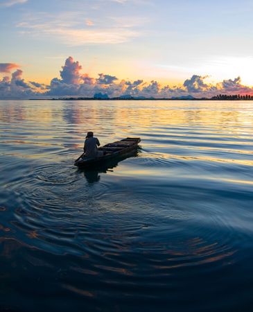 A local fisherman rows his boat during sunrise in the exotic tropical ocean 