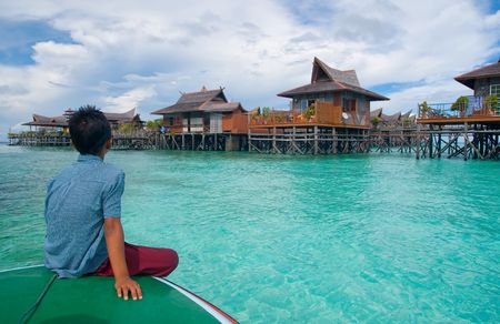 A boy looks at exotic tropical resort in the middle of ocean on crystal clear waterの写真素材