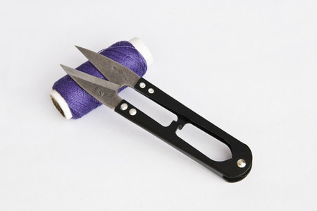 Scissors and a roll of purple thread on white background