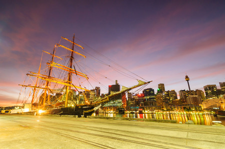 Sydney darling harbour maritime museum and boats at sunrise blurred surrounded by city skyscrapers cloudy red sky and still bay waterのeditorial素材