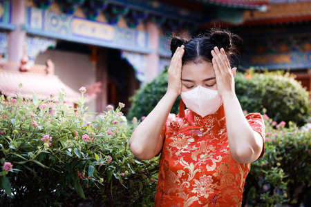 Asian women wear red Chinese clothing, wear masks to prevent germs. She felt sick with a headache...