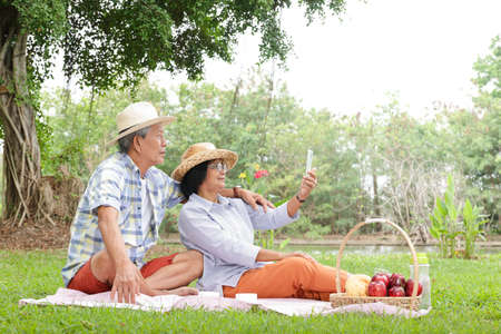 Senior Couple, Asian Husband and Wife Sit and picnic and relax in the park. They are happy in their...