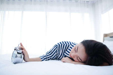 The girl sleeps in bed in the bedroom, the desk clock alarm loudly in the morning She uses her hand...