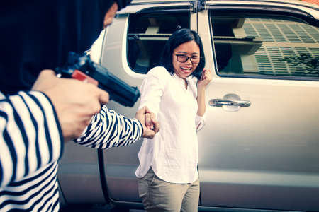 The robbers wore a black mask, carrying a gun, robbing a gold necklace from a woman who was about to open the car door.の写真素材