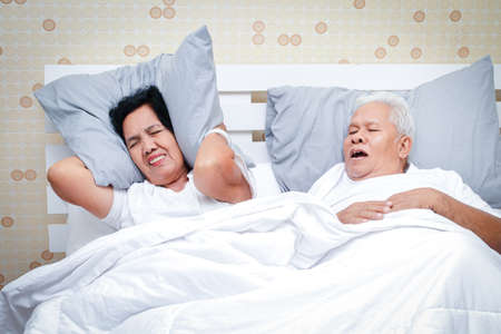 Asian elderly couples Sleeping in bed in the bedroom Men snoring so loudly that women can't sleep. Snoring treatment conceptの写真素材