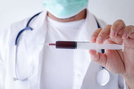 The doctor wears a medical mask and holds a syringe containing the patient's blood to check for epidemics. Treatment hospital conceptの写真素材