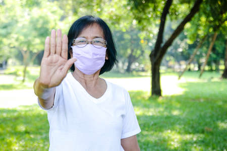Elderly women wear purple cloth masks, raise your hands, do not get close to prevent the spread of the virus. Coronavirus Prevention Concept, Social Distanceの写真素材