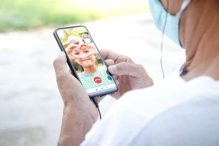 elderly Asian man wearing a mask Use a smartphone to chat with niece via video call. Concept social distance, virus infection preventionの写真素材