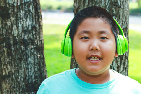 Asian Fat Boy Wearing green music headphones, standing against a happy tree. The concept of child learning developmentの写真素材