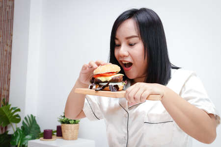 Fat Asian woman eating a hamburger. Full of things that cause diabetes, heart disease, obesity and liver disease. Junk food conceptの写真素材