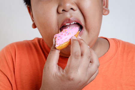 Asian fat boy holds a strawberry-coated donut He enjoys eating. Food concepts that cause children's physical health problems cause diseases. White background.の写真素材