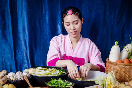 Korean women wearing traditional pink hanboks doing kimchi She is mixing the ingredients in the bowl. To taste delicious. The concept of charming fermented cooking And fragrant, Asian food