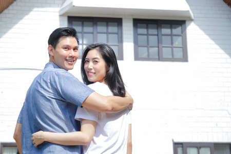 Asian male and female couples stand, hug, and smile happily in front of the new house. The concept of starting a married life In order to create a happy family. copy spaceの写真素材