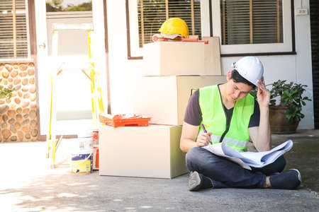 Male engineer inspecting the house Sit and look at the construction plan to check the details...