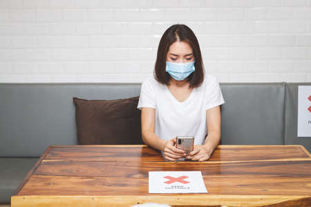 Asian woman wearing a mask Sitting in a restaurant, seat spacing more than 2 meters apart,...