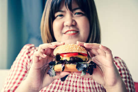 Fat Asian woman eating a hamburger. Full of things that cause diabetes, heart disease, obesity and liver disease.