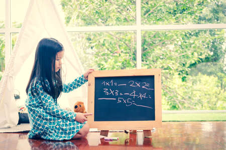 A cute little girl studying mathematics Write the numbers on the black wooden boardの写真素材