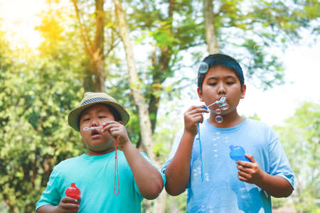 Two boys blowing bubbles in a garden with treesの写真素材