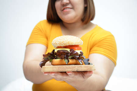 Fat woman wearing a yellow shirt holding a hamburger. Eating health care conceptの写真素材