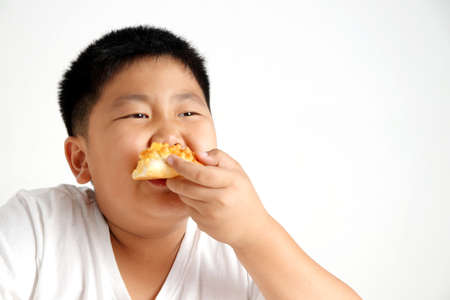 The fat Asian boy is eating a delicious pizza. Concept of eating food for health benefits. White backgroundの写真素材