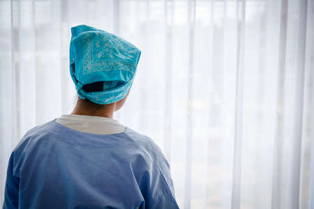 A female cancer patient sits sadly in bed, looking at the window. She is worried about the treatment.の写真素材