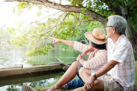 An elderly couple hugging each other with love and happiness in a park with a large pond. Senior community concept, good health, longevityの写真素材