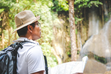 A young man carrying an orange backpack Holding a map paper for traveling
