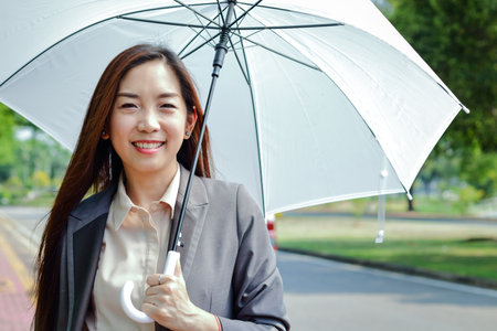 A business woman wearing a suit, she holds a sun-shaded white umbrella. Happy smileの写真素材