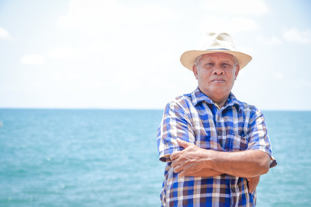 An elderly Asian man wearing a hat to visit the sea to relaxの写真素材