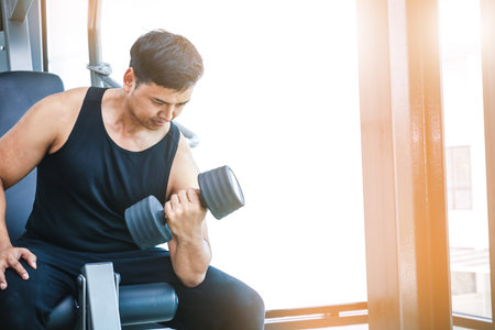 A big Asian guy is lifting a black dumbbell, exercising in the fitness.の写真素材