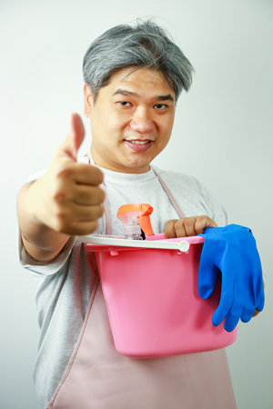 An elderly Asian man carrying a plastic bucket with house cleaning equipmentの写真素材