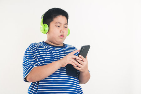 Asian fat boy standing playing smartphone Wearing headphones to music watching him happy. white backgroundの写真素材