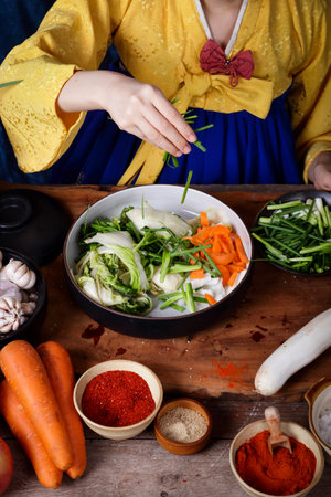 Korean woman wearing traditional hanbok doing kimchi Sprinkle the salt over the fresh vegetables in the bowl. Is a delicious national dish with a pleasant aroma. The concept of Asian fermented cookingの写真素材