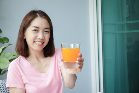 A happy smiling asian woman holding a glass of orange juice Sitting on the front porch. Concept of health problems for women in their 40s. Eat a good and healthy diet.の写真素材