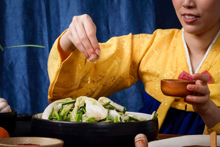 Korean woman wearing traditional hanbok doing kimchi Sprinkle the salt over the fresh vegetables in the bowl. Is a delicious national dish with a pleasant aroma. The concept of Asian fermented cookingの写真素材