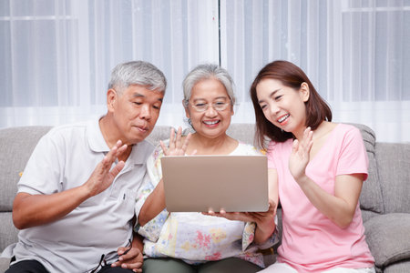 Asian family, parents and daughters online video calling greetings to grandchildren. Via laptop computer At the living room in the house During the coronavirusの写真素材