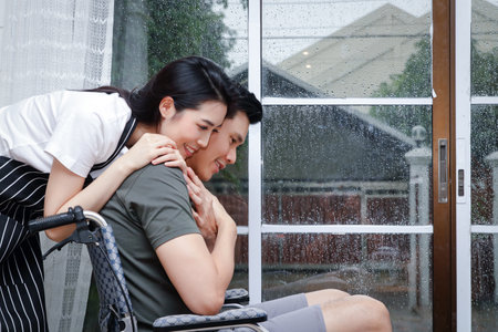 Wife caring for her disabled husband Sitting on a wheelchair in their home. The concept of caring for loved ones in times of illness. Copy spaceの写真素材