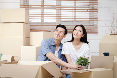 Asian couple moving into a new home Help unpack the brown paper box to decorate the house. Concept of starting a new life, building a family. Copy spaceの写真素材