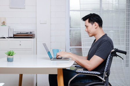 Asian disabled men Ride in a wheelchair Working on a laptop computer At the office in his home. Copy spaceの写真素材