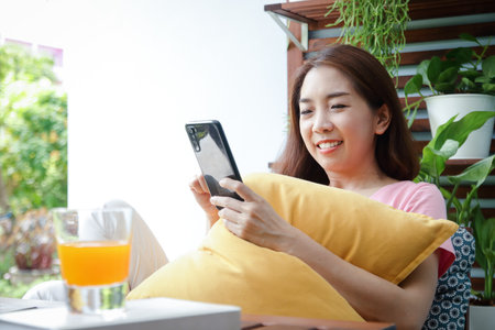 Asian woman, 40 years old Happy holding a smartphone playing social media online On the balcony of her house. Concept of life, health careの写真素材